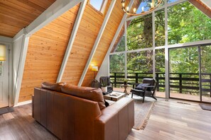 A modern loft bedroom with a sloped ceiling, large windows, and a cozy seating area. - Black Butte Ranch A-Frame · Pools, Golf, Sleeps 8 (Sisters)