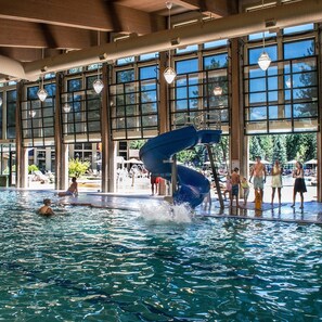 Una piscina interior con tobogán de agua, amplias ventanas y una zona cubierta con sillones de descanso.
