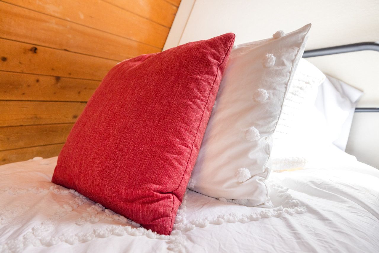 A bed with white bedding and two pillows, one red and one white, in a room with wooden paneling.