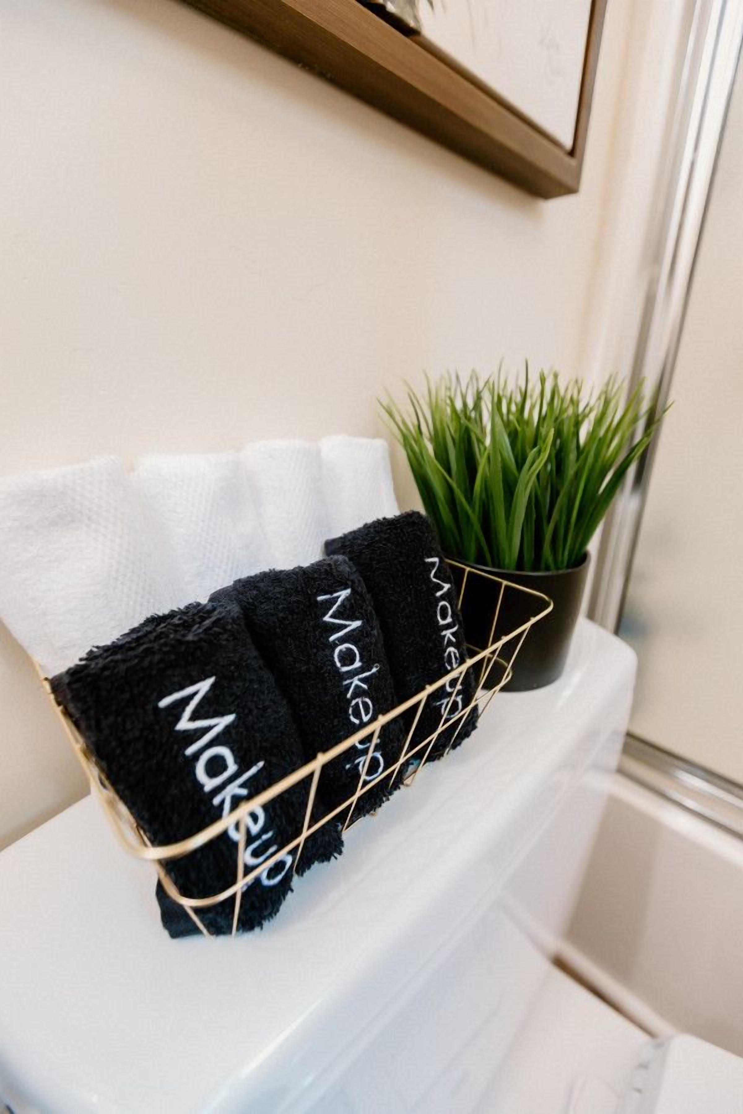 A bathroom with a white toilet, a black towel rack with towels, and a potted plant.