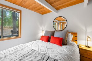 Un dormitorio con un ventanal grande, un espejo redondo, un cabecero de madera y una mesita de noche con una lámpara.
