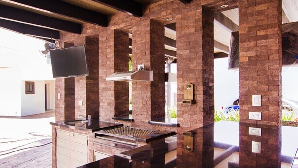 An outdoor kitchen with a brick wall, a flat-screen TV mounted above the counter, and a chimney. - Amplio departamento, con la mejor ubicación en la ciudad (Chihuahua)