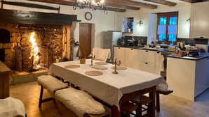 A cozy kitchen with a stone fireplace, wooden beams, and a dining area with a table set for four. - Large family gîte in Auvergne, 5 bedrooms, linen included, sleeps 12,  (Fayet-Ronaye)