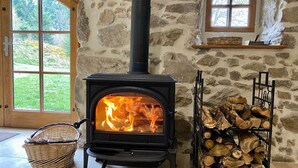 A stone fireplace with a black stove, a window, and a log shelf. - Large family gîte in Auvergne, 5 bedrooms, linen included, sleeps 12,  (Fayet-Ronaye)