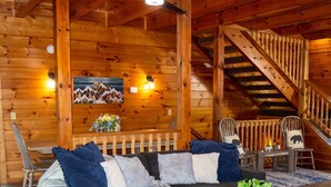 A log cabin interior with a sofa set, a dining table, chairs, a staircase, and a mountain painting on the wall. - Stop Booking 2 Cabins. This One Sleeps 34. (Pigeon Forge)