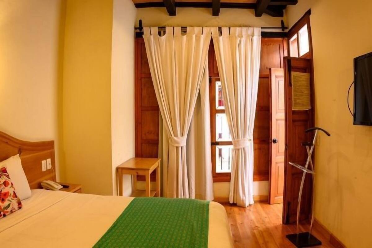 A bedroom with a wooden bed, a small bedside table, a green throw blanket, and a wooden floor.