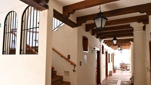Un couloir avec un escalier en bois, une grille en fer forgé et une charrette visible au loin.