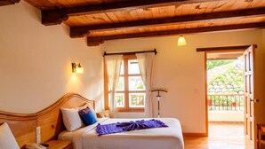 Une chambre avec deux lits, des poutres en bois au plafond, une fenêtre avec des rideaux et une porte donnant sur l’extérieur.