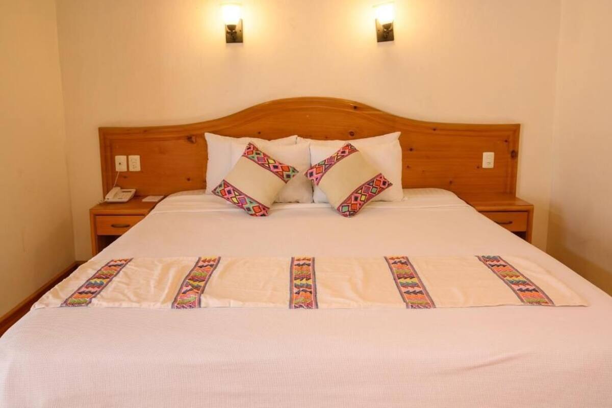 A neatly made bed with a wooden headboard, two bedside tables with lamps, and a wall-mounted phone.