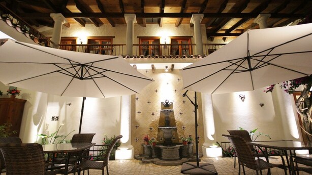 Un espace extérieur aménagé en terrasse, avec des tables et des chaises sous des parasols, une fontaine et un sol carrelé.