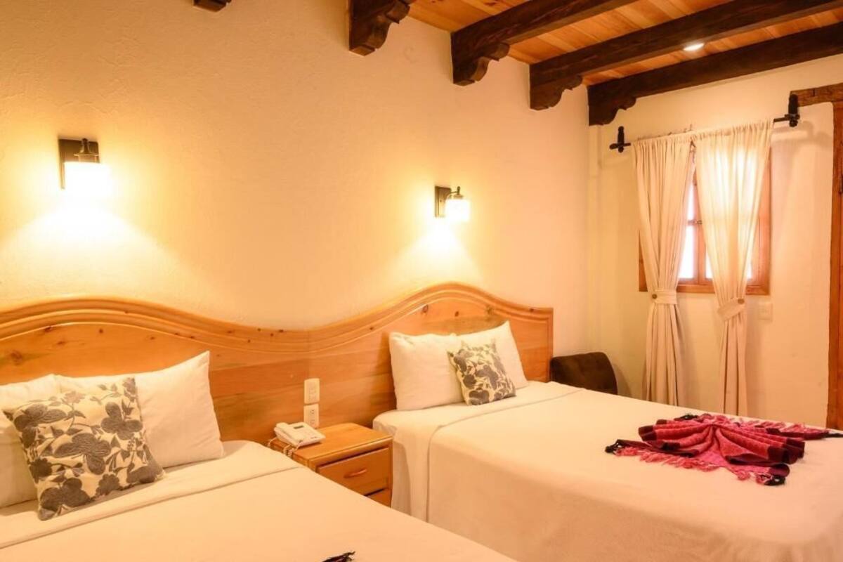 A hotel room with two beds, wooden headboards, bedside lamps, a telephone, and a window with curtains.