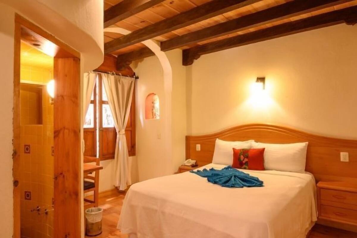 A bedroom with a wooden headboard, a bedside table with a lamp, and a window with curtains.