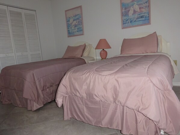 A bedroom with two beds, a nightstand, a lamp, and two wall-mounted paintings.