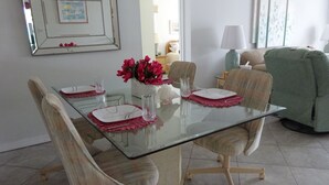 En matplats med ett glasbord, fyra stolar och en vas med röda blommor.