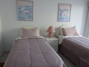 A bedroom with two beds, each with a white headboard and a pink pillow. There is a nightstand with a pink lamp between the beds.