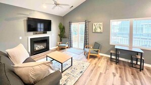 A modern living room with a fireplace, seating area, and large windows. - Charming, Beautiful, Treetop Loft, Prime Location (Wilmington)