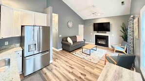 A modern kitchen with stainless steel appliances, a gray sofa, a flat-screen TV, and a fireplace. - Charming, Beautiful, Treetop Loft, Prime Location (Wilmington)