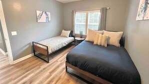 A bedroom with two beds, a ceiling fan, a window with curtains, and artwork on the walls. - Charming, Beautiful, Treetop Loft, Prime Location (Wilmington)