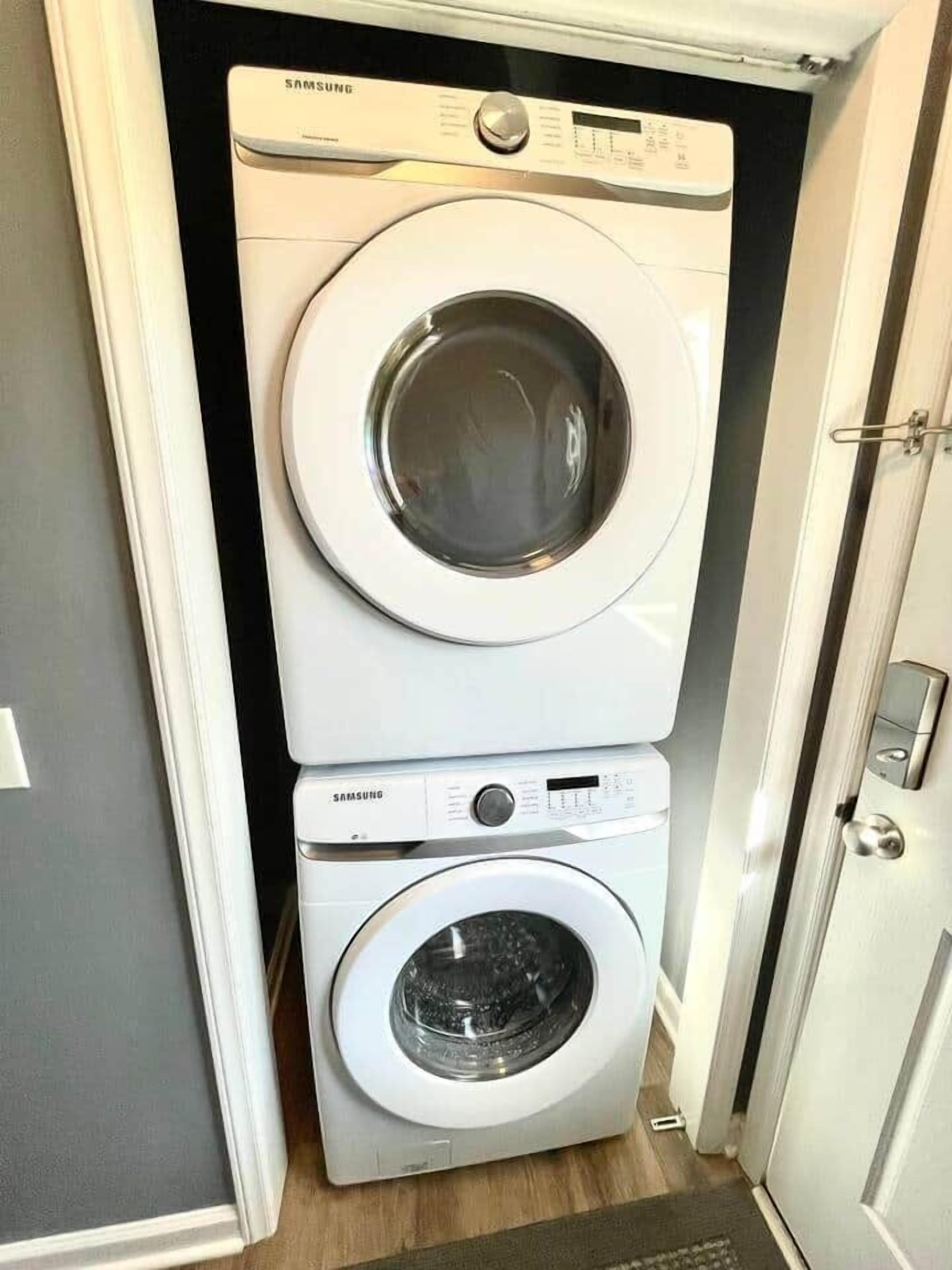Una lavadora y secadora Samsung apiladas en un espacio reducido, con una puerta a la derecha.
