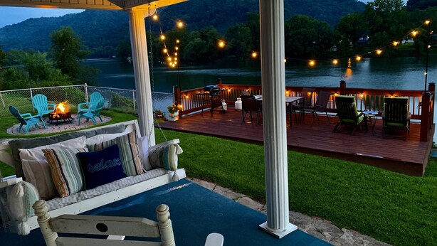 Eine überdachte Terrasse mit Sitzgelegenheiten im Freien, einem Feuerkorb und Blick auf einen See und Berge.