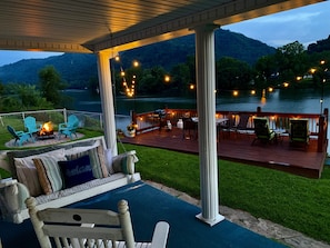 A covered deck with outdoor seating, a fire pit, and a view of a lake and mountains.