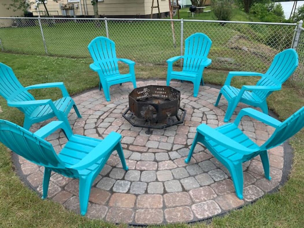 Een rond zitgedeelte buiten met zes turquoise Adirondack-stoelen rond een vuurkuil.