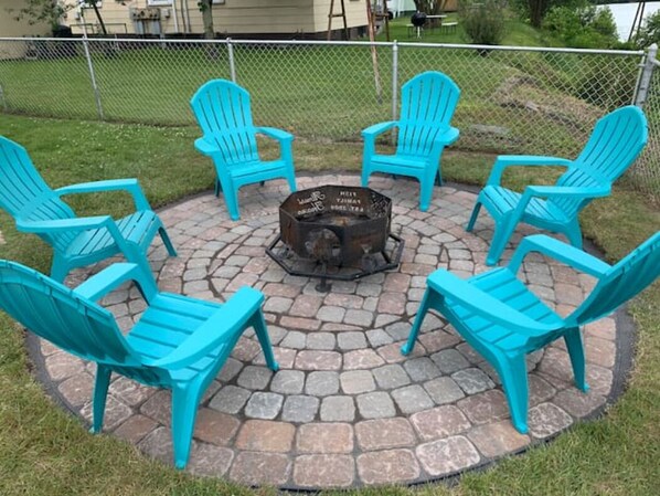 A circular outdoor seating area with six turquoise Adirondack chairs around a central fire pit.