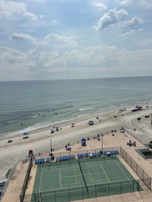 A beach with a tennis court, umbrellas, and beach chairs.
