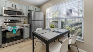 Een moderne keuken met roestvrijstalen apparatuur, een eettafel met placematen en een raam met zonwering.