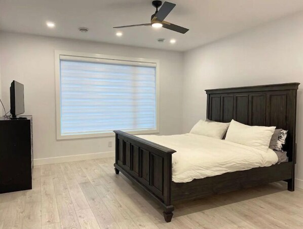 A bedroom with a bed, a ceiling fan, a window with blinds, and a TV on a stand.