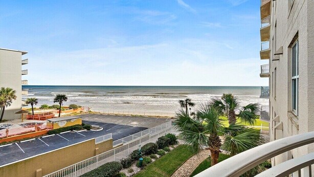 Blick auf den Strand vom Balkon aus, mit blauem Himmel, Parkplatz und Palmen.