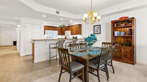 Ein Essbereich mit einem Holztisch, Stühlen und einer Chandelier. Im Hintergrund ist eine Küche mit Holzschränken und einem Kühlschrank zu sehen.
