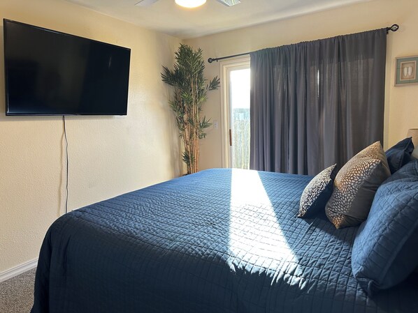 A bedroom with a bed, a television mounted on the wall, a plant, and a window with curtains.