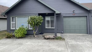 Una casa residencial con fachada gris oscuro, puerta de garaje verde y un pequeño árbol en el jardín delantero.