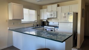Una cocina con armarios blancos, una isla con encimera de vidrio, estufa, microondas y refrigerador.