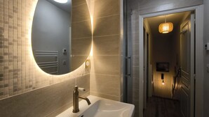 Een badkamer met een grote spiegel in ovaalvorm, een witte wastafel en een douchegedeelte.