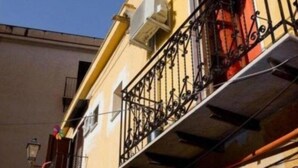 A building with a yellow facade, black wrought iron balcony railing, and a visible window with a white awning. - Teatro Massimo Apartament self check-in (Palermo)