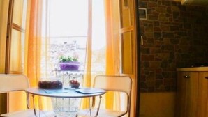 A corner of a room with a table and chairs, a window with curtains, and a stone wall. - Teatro Massimo Apartament self check-in (Palermo)
