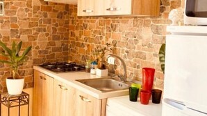 A kitchen with a stone wall, wooden cabinets, a gas stove, a sink, and a microwave. - Teatro Massimo Apartament self check-in (Palermo)