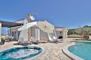 Un espace aménagé au bord de la piscine, avec des chaises longues, des parasols et un jacuzzi.