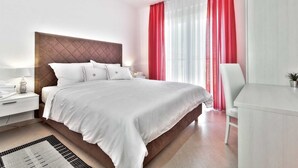 A modern hotel room with a large bed, a bedside table with a lamp, a desk with a chair, and a window with red curtains. - Casa Siesta with swimming pool, jacuzzi & garage (Štrika (Istria))