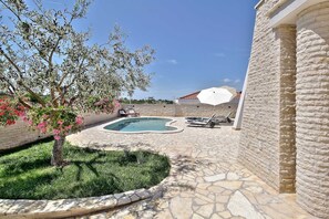A stone pool with lounge chairs, a white umbrella, and a tree with pink flowers. - Casa Siesta with swimming pool, jacuzzi & garage (Štrika (Istria))