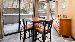 A dining area with a wooden table and chairs, a wooden cabinet, and a large window with a view of a snowy outdoor area. - Silver King 206 | 150 Yards to Lifts | Fireplace | Kitchen | Pool & Hot Tub (Park City)