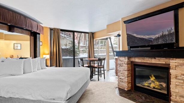 A hotel room with a large bed, a fireplace, a television, and a view of snowy mountains. - Silver King 206 | 150 Yards to Lifts | Fireplace | Kitchen | Pool & Hot Tub (Park City)