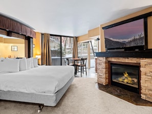 Ett hotellrum med en stor säng, en öppen spis, en tv och utsikt över snöklädda berg.