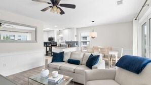 A modern living room with a sofa, coffee table, and a dining area in the background.