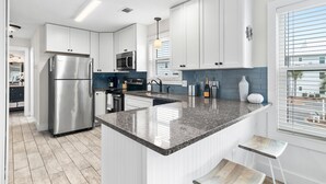 A modern kitchen with white cabinets, stainless steel appliances, a granite countertop, and a view of the outdoors through a window.