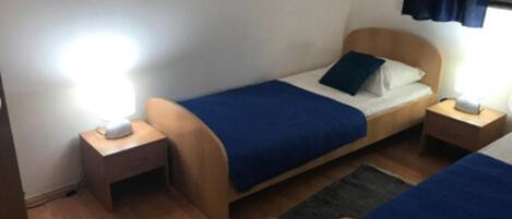 A small, neatly arranged bedroom with two single beds, wooden headboards, and bedside tables with lamps.