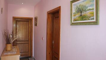 A hallway with a wooden door, a framed painting, and a desk with a vase of dried plants.