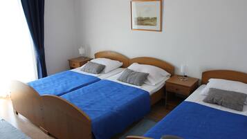 Een tweepersoonskamer met twee bedden, elk met een blauwe spreideken en kussens, houten hoofdeinden, nachtkastjes met lampen en een ingelijst schilderij aan de muur.